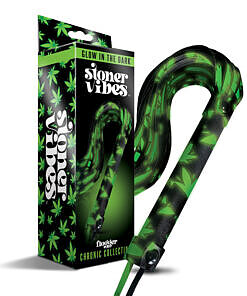 Black cannabis-embossed faux leather flogger glowing green in the dark on a bedroom surface.