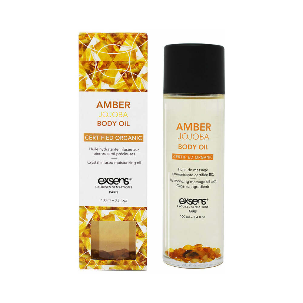 Exsens Amber Jojoba Body Oil 3.4 oz bottle on a spa table with soft floral accents and warm amber tones.