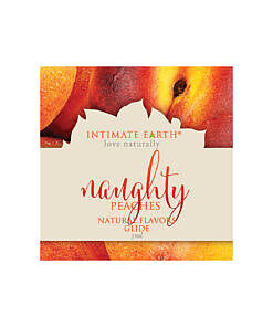 Intimate Earth Naughty Peach lubricant foil packet next to a ripe peach on a clean white surface.