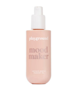 Playground Mood Maker Body & Massage Oil bottle with pump on a bed with fresh flowers